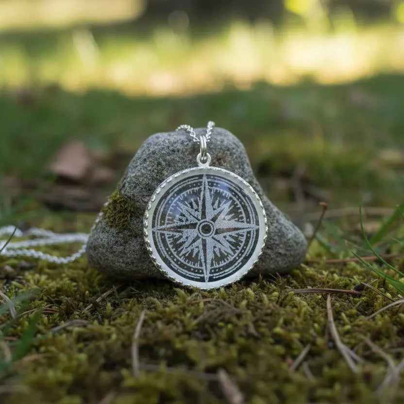 Silver compass pendant necklace on a stone with a natural background